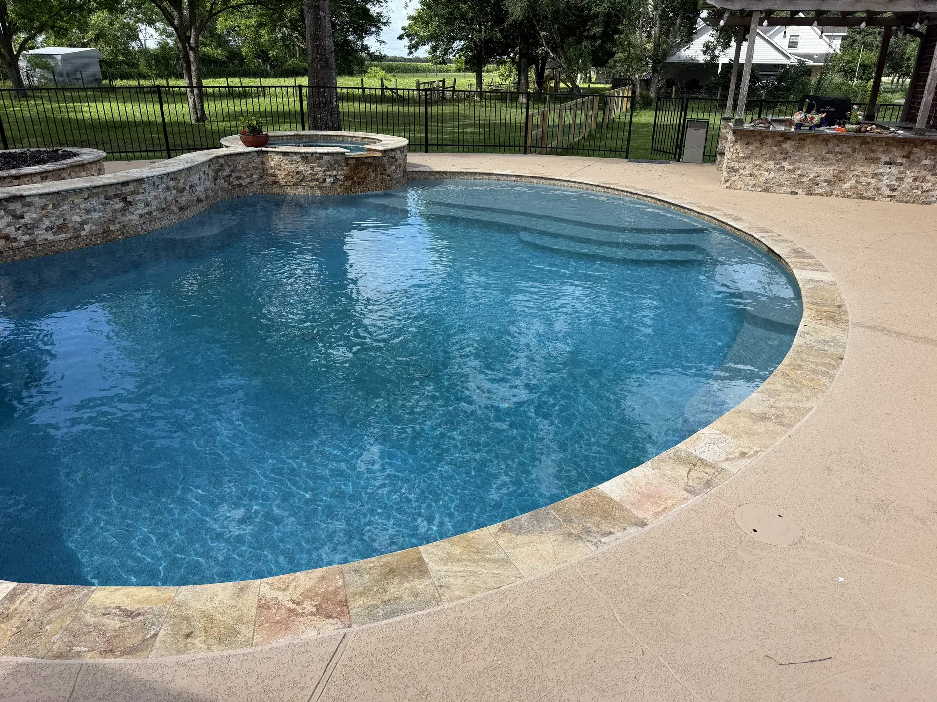 Custom freeform gunite pool with raised stacked-stone spa and travertine tanning ledge built by Venture Pool Company